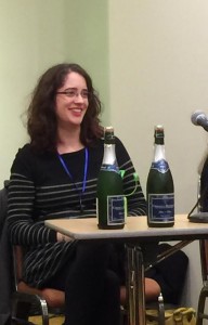 A woman seated behind a table with two bottles of champagne at a book launch