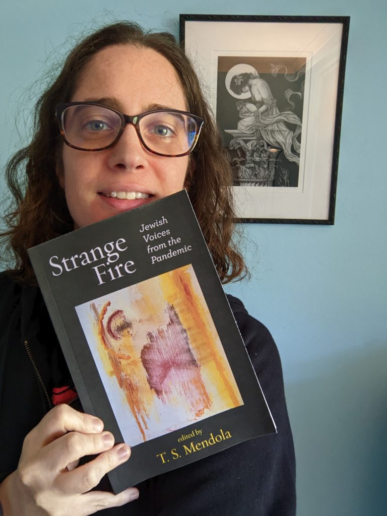 Rivqa is smiling and holding a copy of Strange Fire