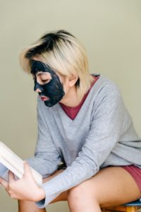 Stock image of a blonde person who is reading with a charcoal face mask on